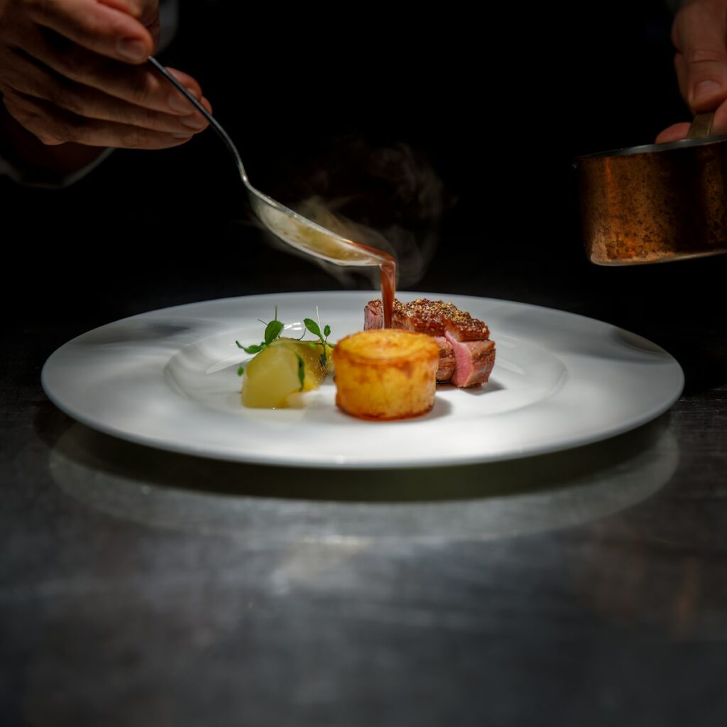 Chef spooning sauce over a plated steak