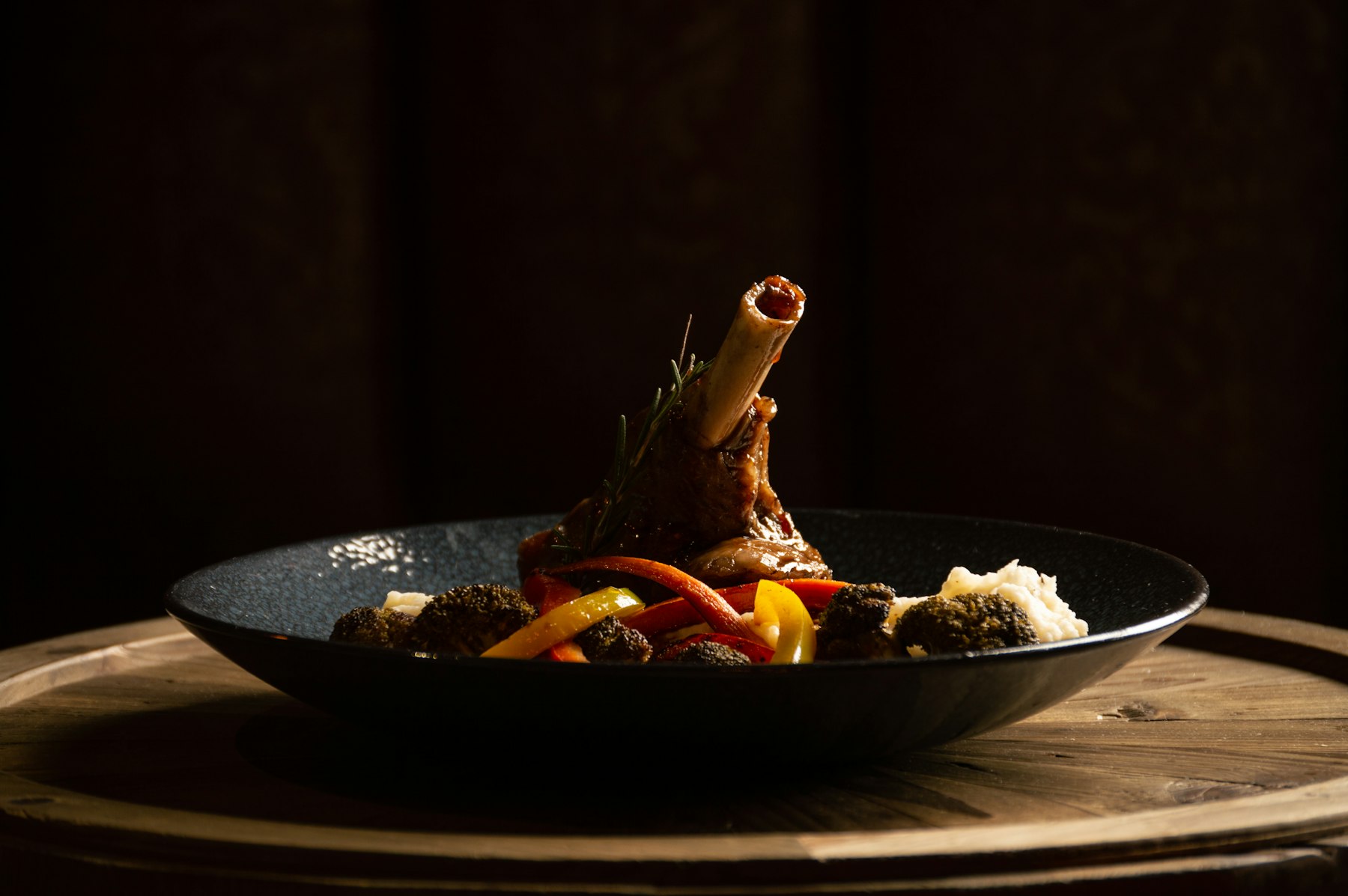 Braised lamb shank with root vegetables on a wooden table at Harvest & Oak